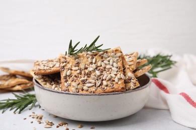 Photo of Cereal crackers with flax, sunflower, sesame seeds and rosemary in bowl on light table, closeup