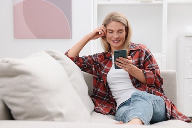 Photo of Happy woman sending message via smartphone on couch at home