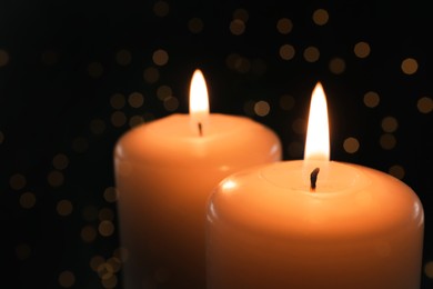 Image of Wax candles burning on black background with blurred lights, closeup. Bokeh effect