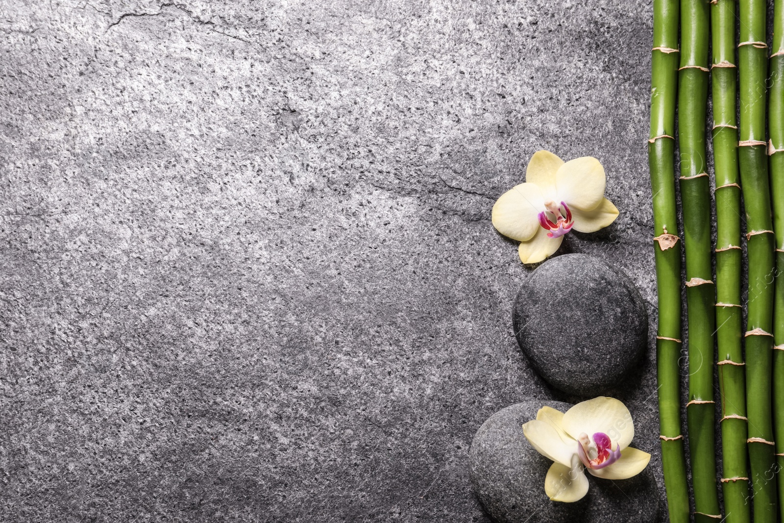 Photo of Spa stones, beautiful orchid flowers and bamboo stems on grey table, flat lay. Space for text