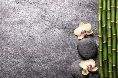 Photo of Spa stones, beautiful orchid flowers and bamboo stems on grey table, flat lay. Space for text