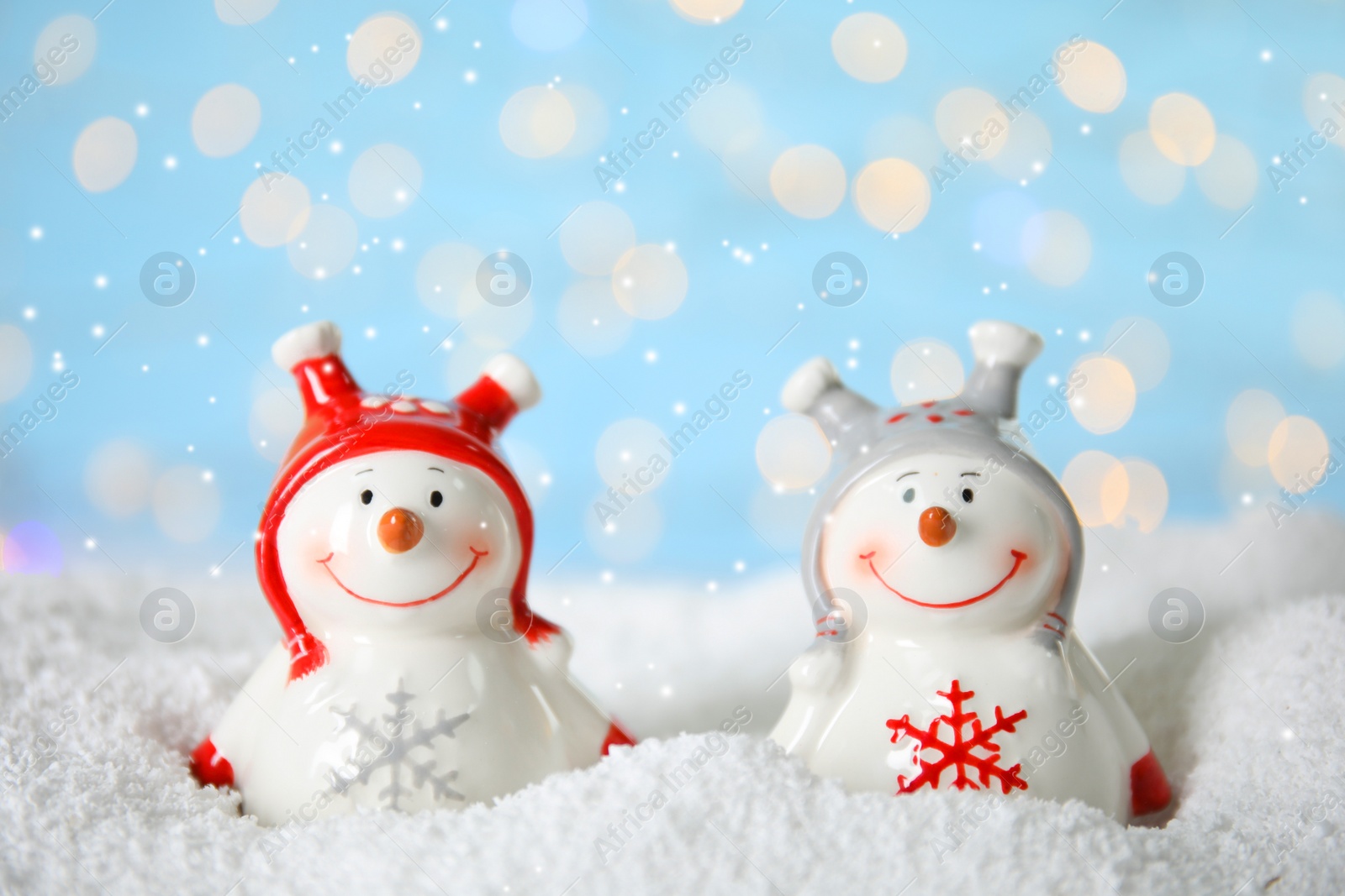 Photo of Decorative snowmen on artificial snow against blurred festive lights