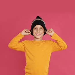Photo of Cute little boy in warm hat on pink background. Winter season