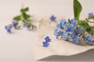 Photo of Beautiful Forget-me-not flowers and parchment on white wooden table, closeup. Space for text
