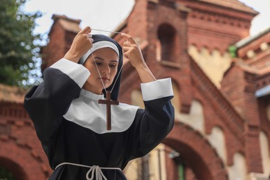 Photo of Young nun wearing Christian cross near building outdoors