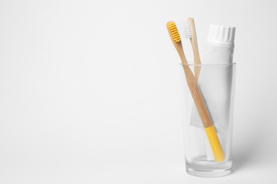 Photo of Glass with brushes and toothpaste on white background. Space for text