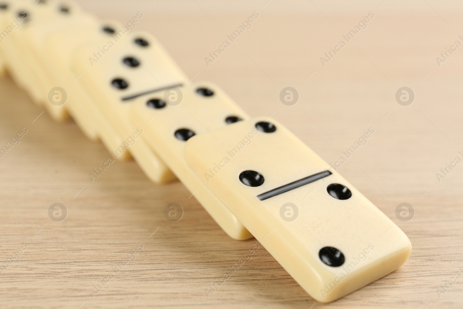 Photo of Fallen white domino tiles on wooden table, closeup
