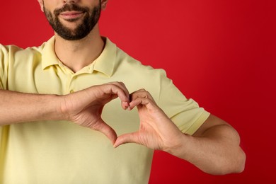 Photo of Man making heart with hands on red background, closeup