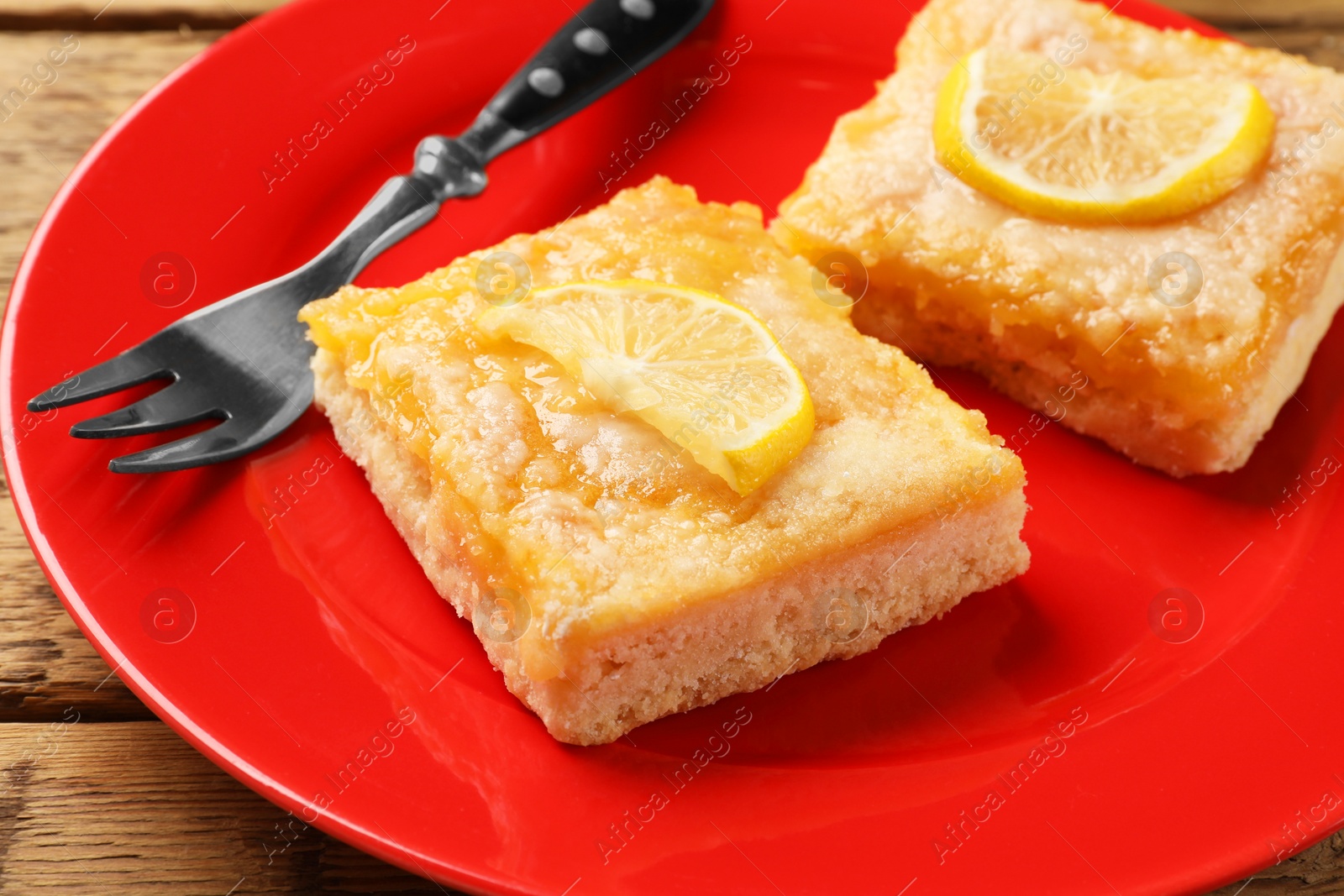 Photo of Tasty lemon bars and fork on wooden table, closeup