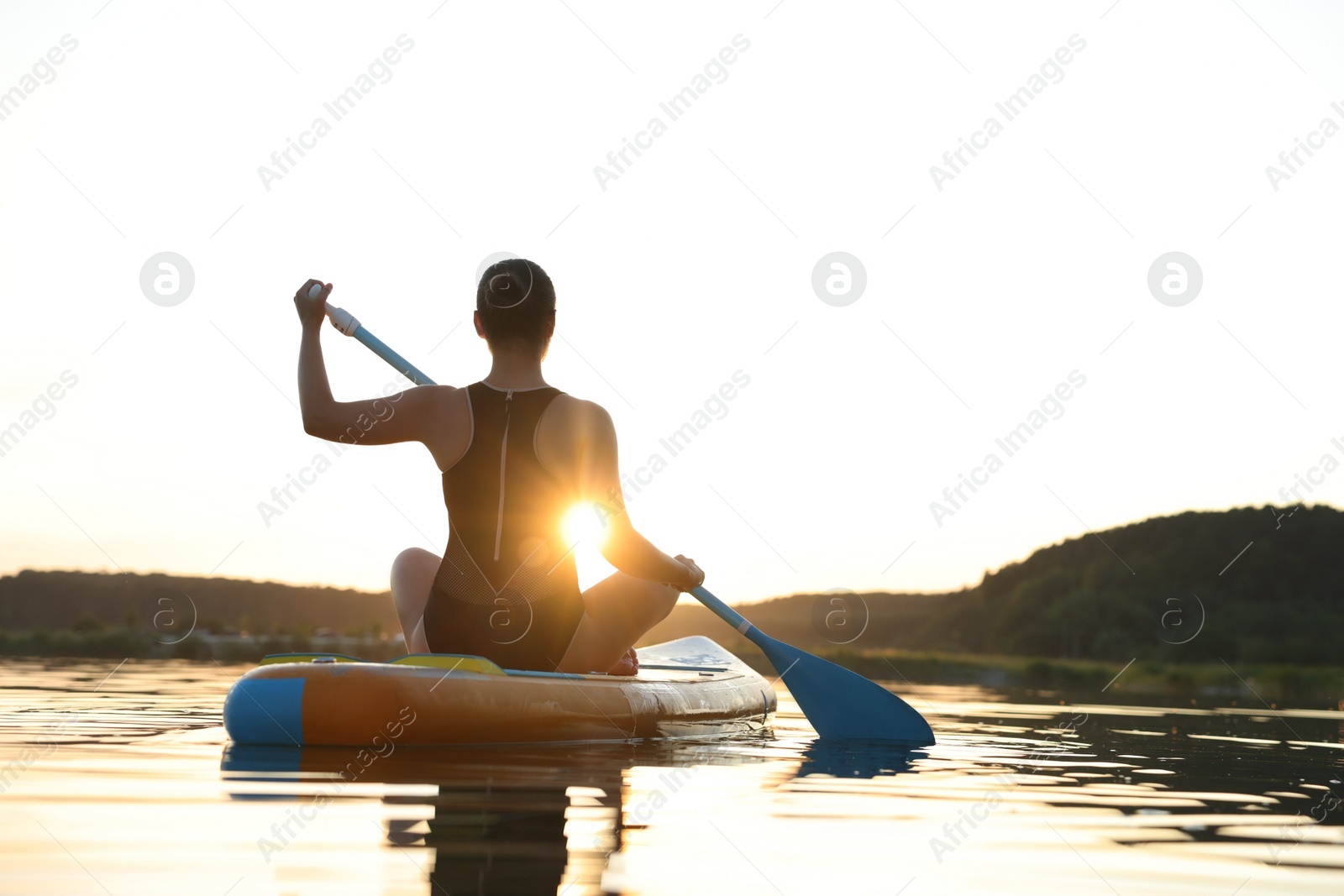 Photo of Woman paddle boarding on SUP board in river at sunset, back view