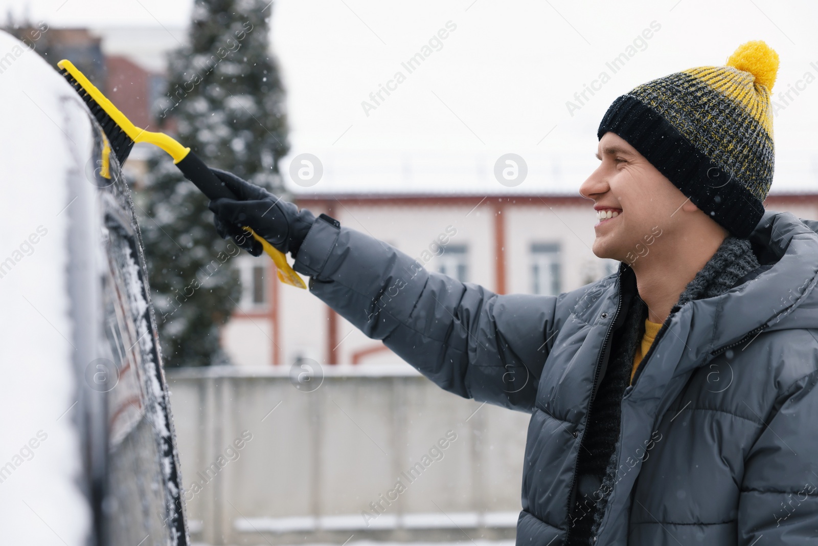 Photo of Man cleaning snow from car with brush outdoors