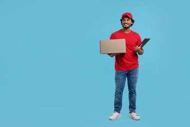 Photo of Happy courier with parcel and clipboard on light blue background, space for text