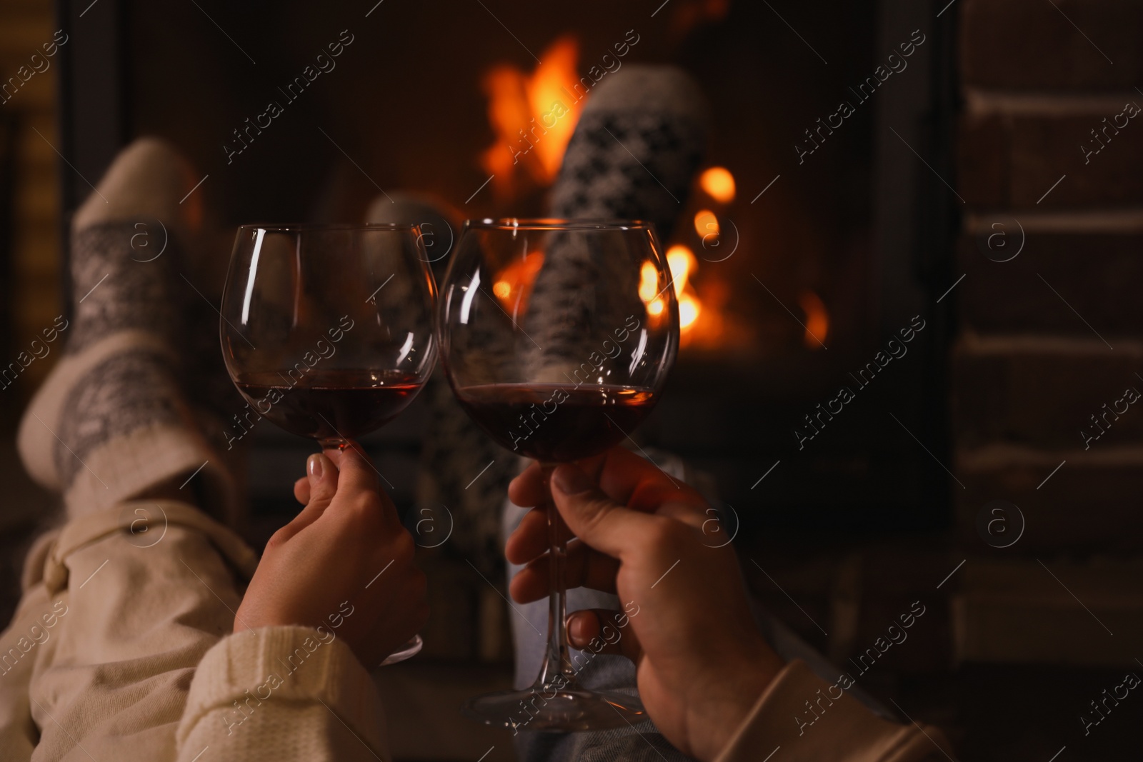 Photo of Couple with glasses of red wine near burning fireplace, closeup