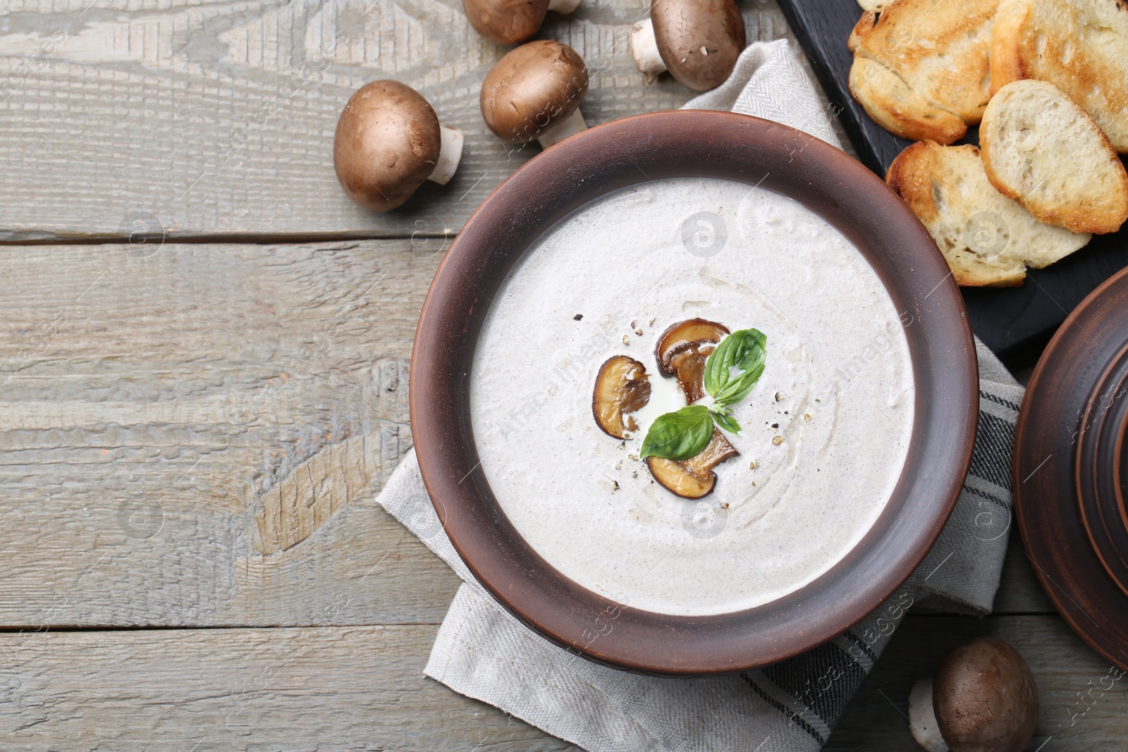 Photo of Delicious homemade mushroom soup in ceramic pot and fresh ingredients on wooden table. Space for text