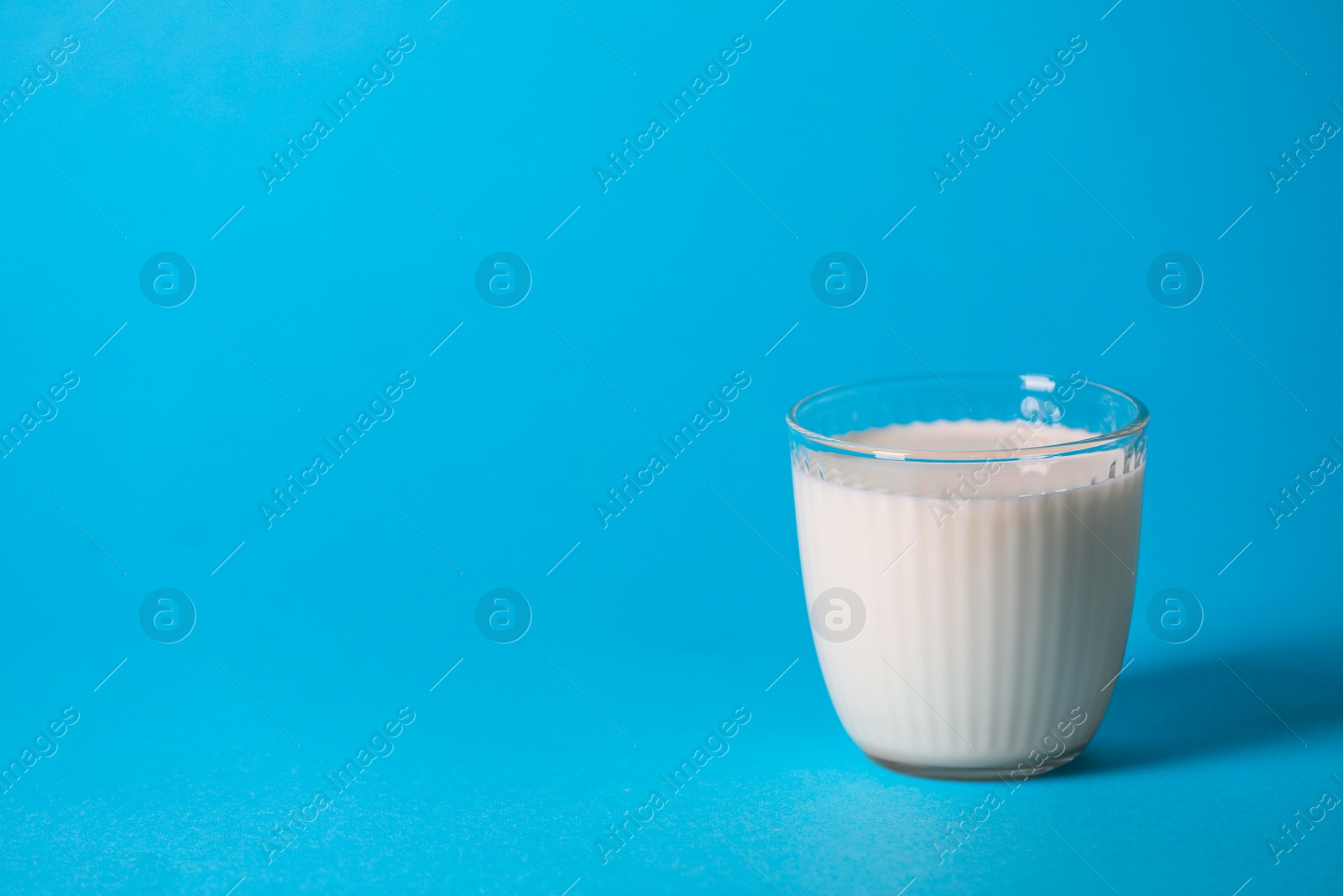 Photo of Tasty fresh milk in glass on light blue background, space for text