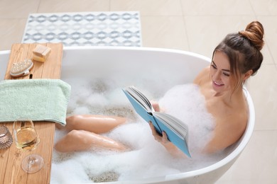 Beautiful woman reading book while enjoying bubble bath at home