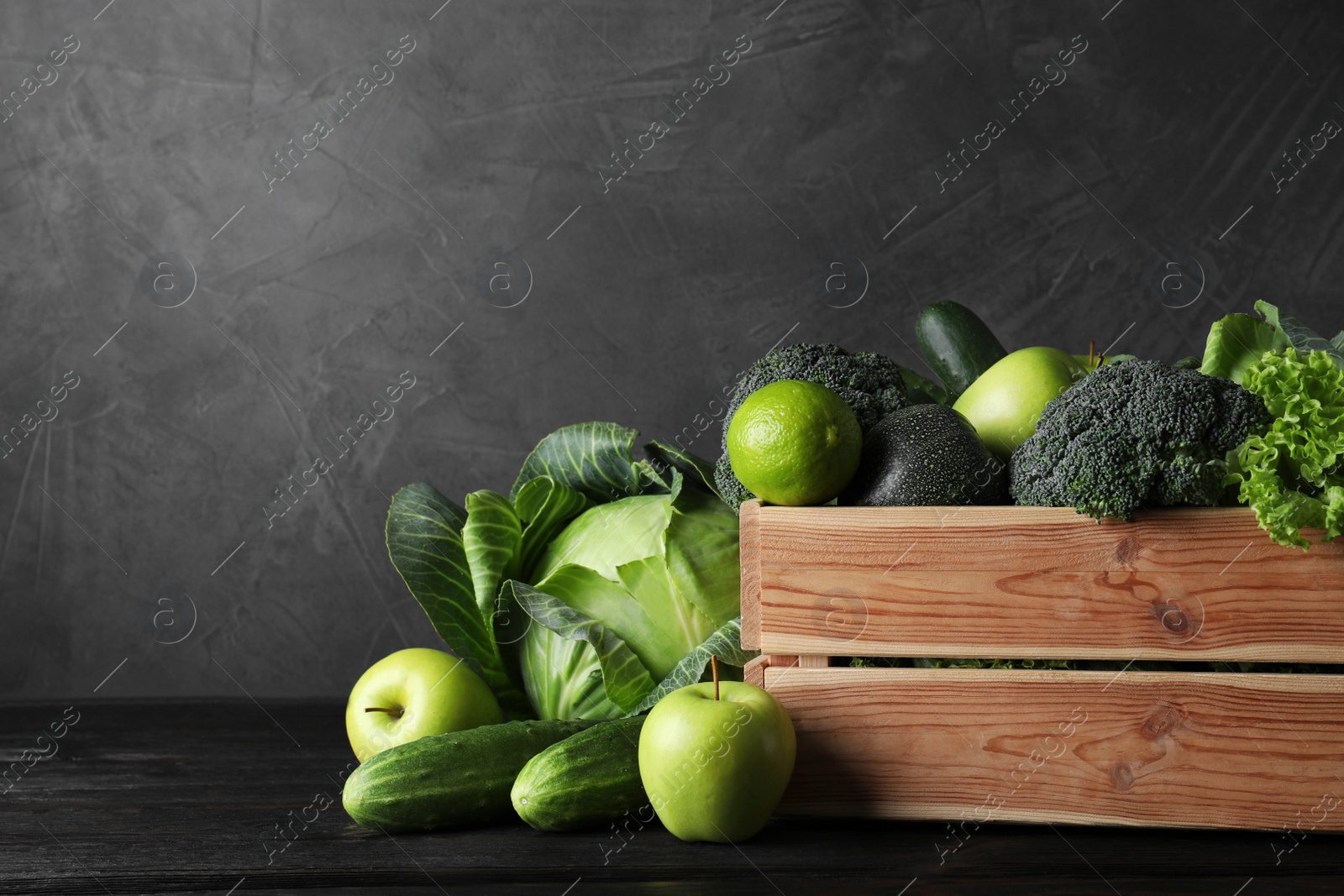 Photo of Wooden crate, fresh green fruits and vegetables on dark background. Space for text