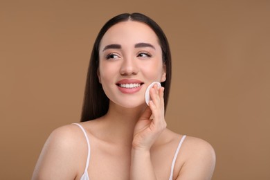 Photo of Beautiful woman removing makeup with cotton pad on beige background