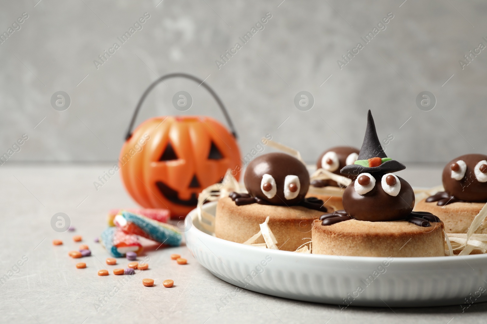 Photo of Delicious biscuits with chocolate spiders on light grey table. Halloween celebration