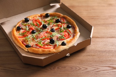 Photo of Cardboard box with tasty pizza on wooden table