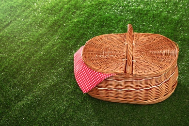 Closed picnic basket with napkin on grass, space for text