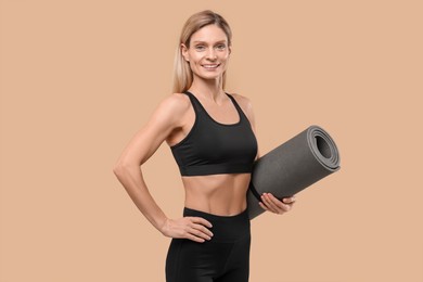 Athletic woman with fitness mat on beige background