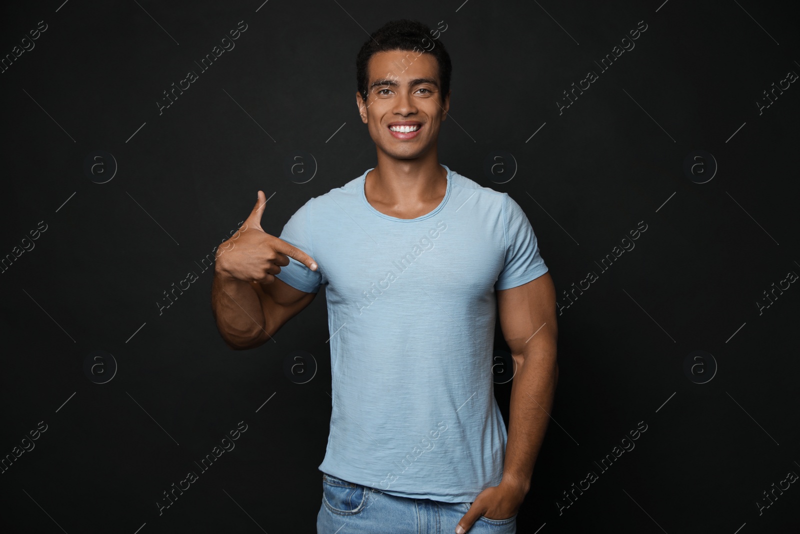 Photo of Handsome young African-American man in blank t-shirt on black background. Space for design