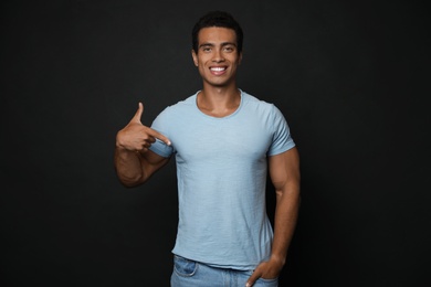 Photo of Handsome young African-American man in blank t-shirt on black background. Space for design