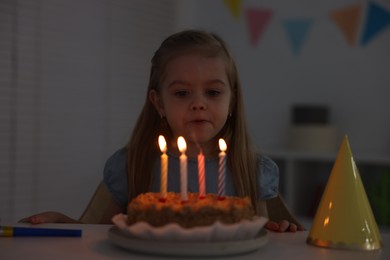 Photo of Cute girl with birthday cake at table indoors