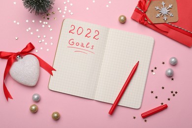 Photo of Planning goals for 2022 New Year. Notebook and festive decor on pink background, flat lay