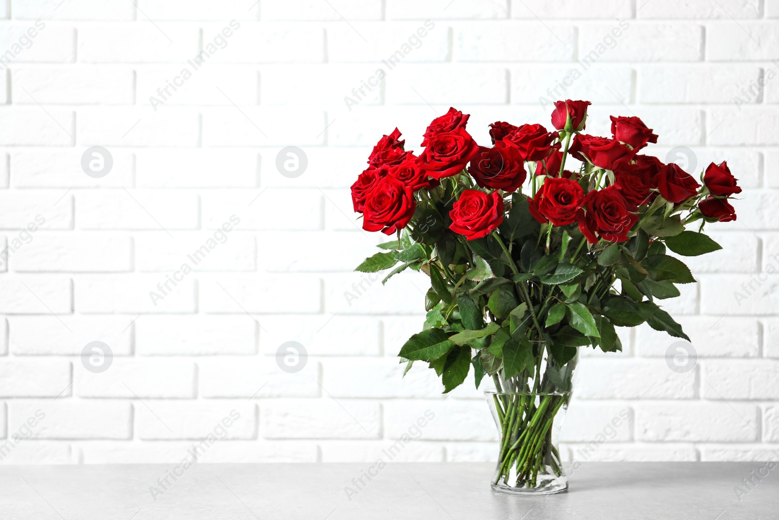 Photo of Vase with beautiful red roses on table against brick wall background