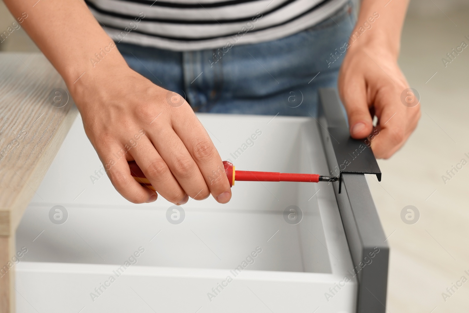 Photo of Woman with screwdriver assembling drawer, closeup view