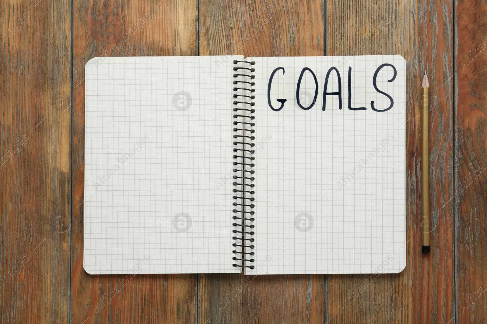 Photo of Notebook with goal list and pencil on wooden table, flat lay