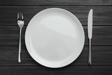 Photo of Empty plate, fork and knife on black wooden table, top view