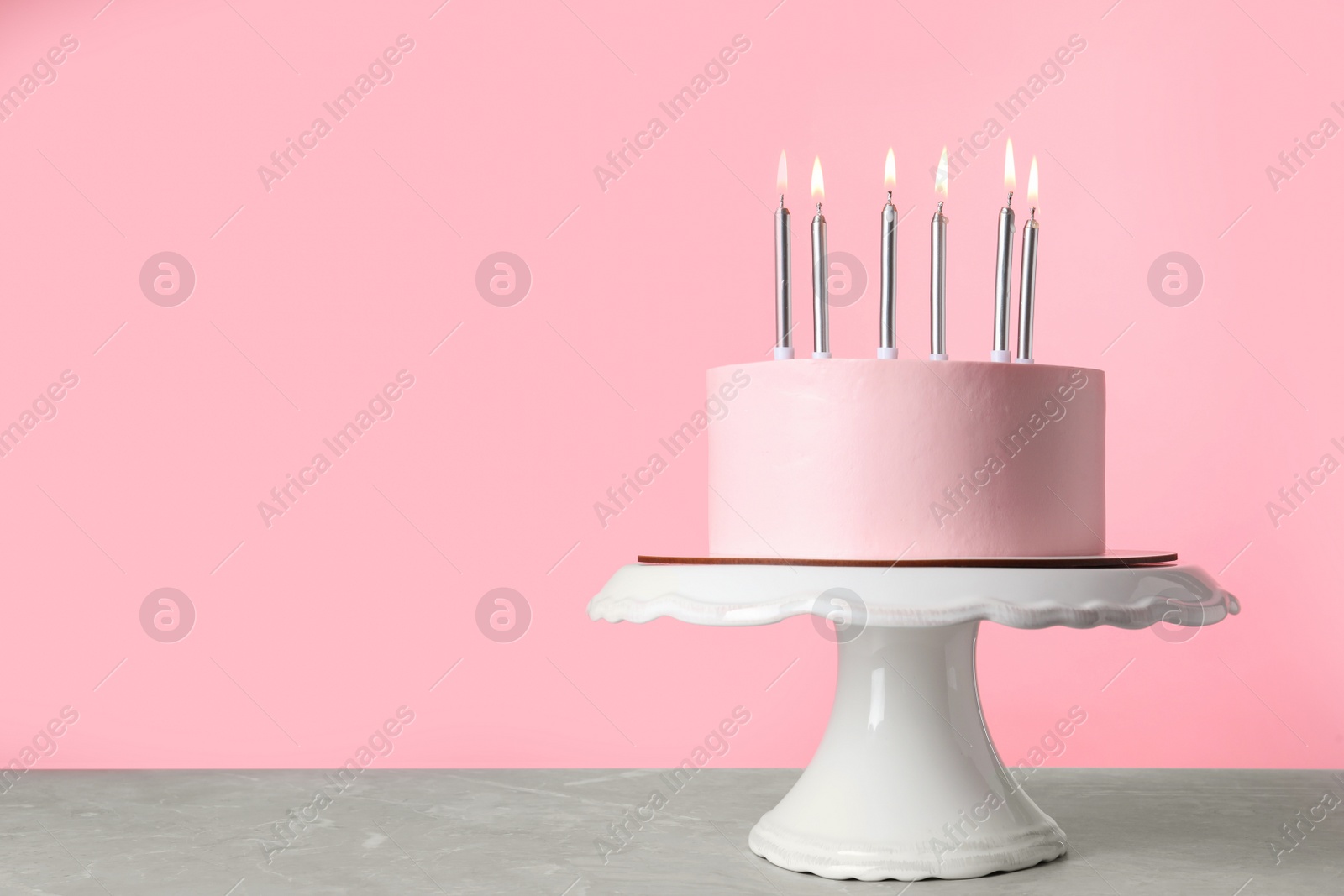 Photo of Birthday cake with burning candles on table against pink background, space for text