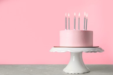 Photo of Birthday cake with burning candles on table against pink background, space for text