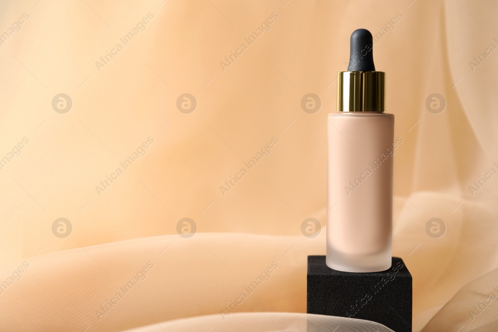 Photo of Bottle of skin foundation on beige tulle fabric, space for text. Makeup product