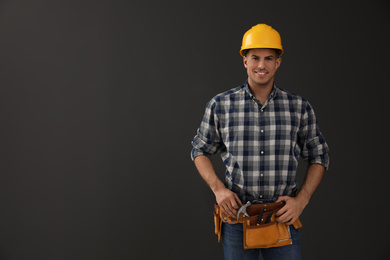 Photo of Handsome carpenter with tool belt on dark background. Space for text