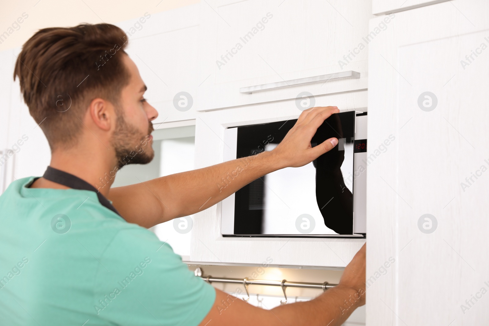 Photo of Young man using modern microwave oven at home