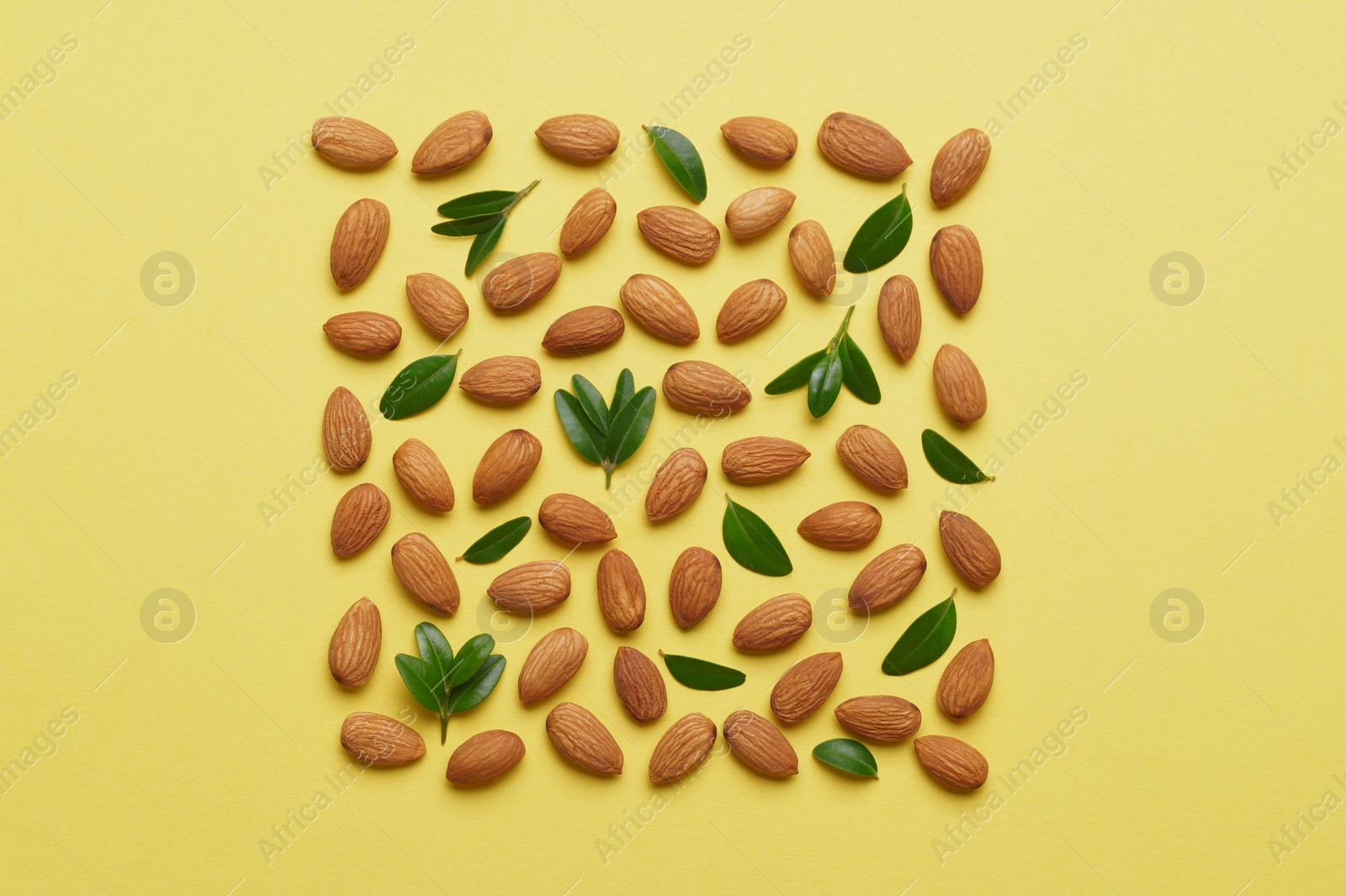 Photo of Delicious almonds and fresh leaves on yellow background, flat lay