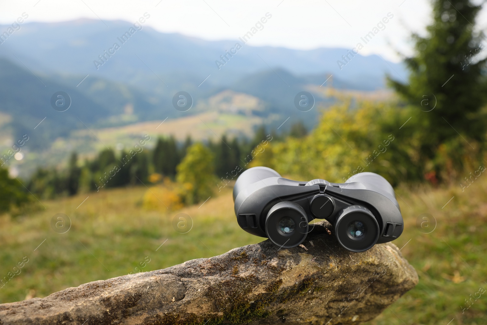 Photo of Modern binoculars on stone in mountains, space for text
