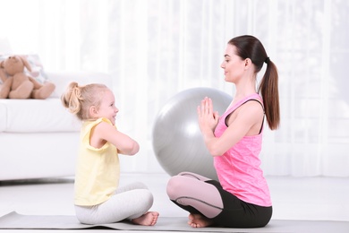 Sportive woman doing fitness exercises with daughter at home