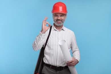 Photo of Architect in hard hat holding draft showing ok gesture on light blue background