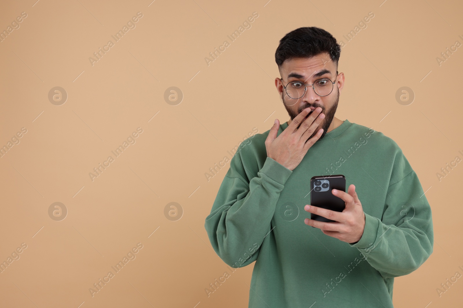 Photo of Shocked young man using smartphone on beige background, space for text