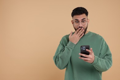 Shocked young man using smartphone on beige background, space for text