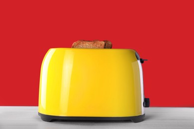 Photo of Modern toaster with slices of roasted bread on white wooden table