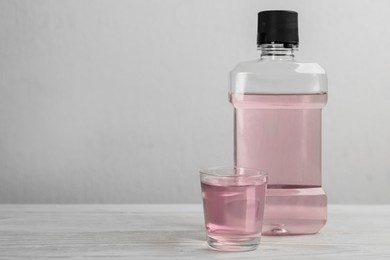 Bottle and glass with mouthwash on white wooden table, space for text