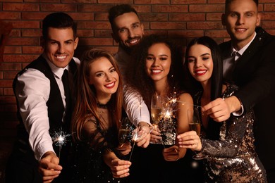 Photo of Happy friends with glasses of sparkling wine and sparklers celebrating New Year indoors