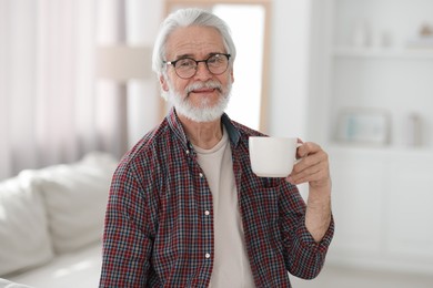 Portrait of happy grandpa with glasses and cup of drink indoors