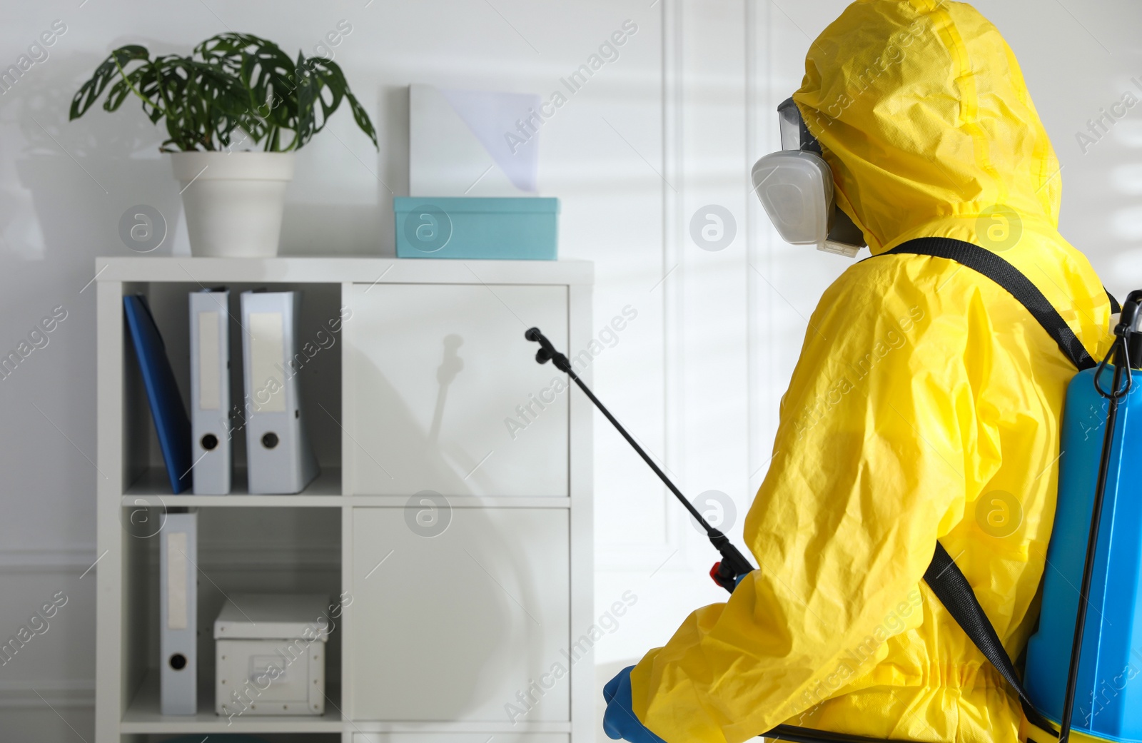 Photo of Employee in protective suit sanitizing office. Medical disinfection